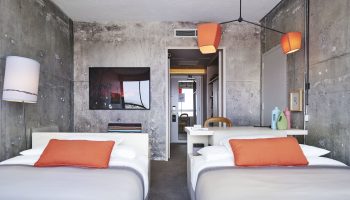 The Linq Hotel and Casino room with two beds, concrete walls, and orange accents. A gay-friendly hotel option in Las Vegas.
