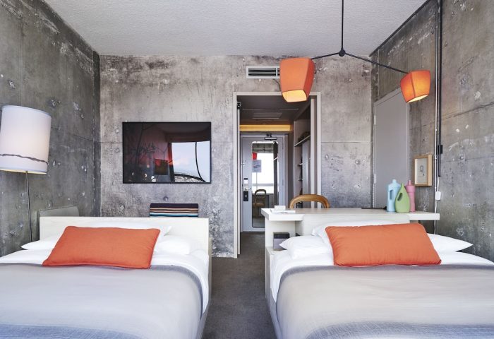 The Linq Hotel and Casino room with two beds, concrete walls, and orange accents. A gay-friendly hotel option in Las Vegas.