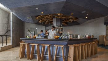 Bar at The Linq Hotel & Casino, a gay-friendly hotel. Bartenders, wooden stools, and a modern ceiling design create a stylish, welcoming vibe.