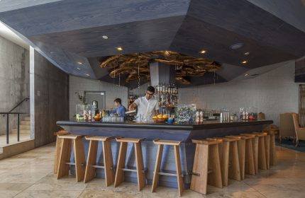 Bar at The Linq Hotel & Casino, a gay-friendly hotel. Bartenders, wooden stools, and a modern ceiling design create a stylish, welcoming vibe.