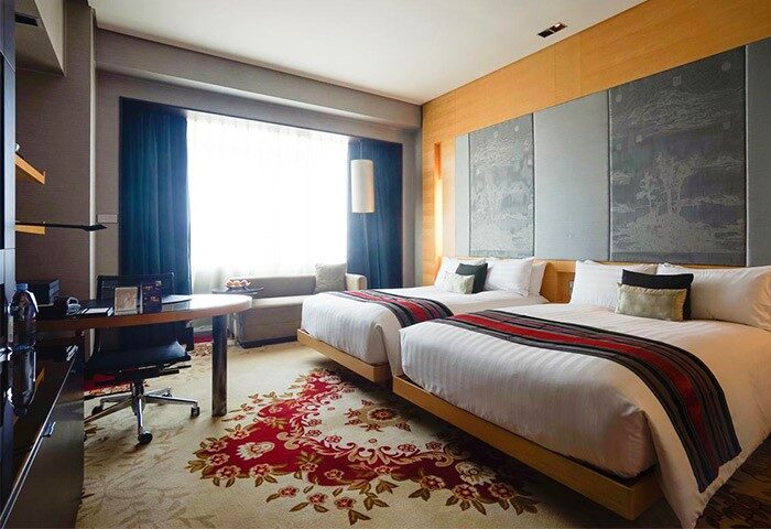 The Longemont Shanghai Hotel room with twin beds. Gay-friendly hotel with a desk, floral carpet, and seating area. Shanghai travel advice.