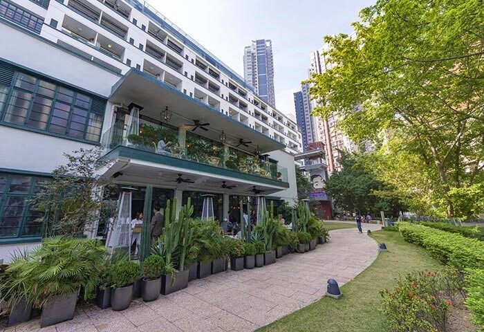 The Mercer Hong Kong, a gay-friendly hotel. Exterior view of the hotel's restaurant with outdoor seating and lush greenery. Modern architecture.