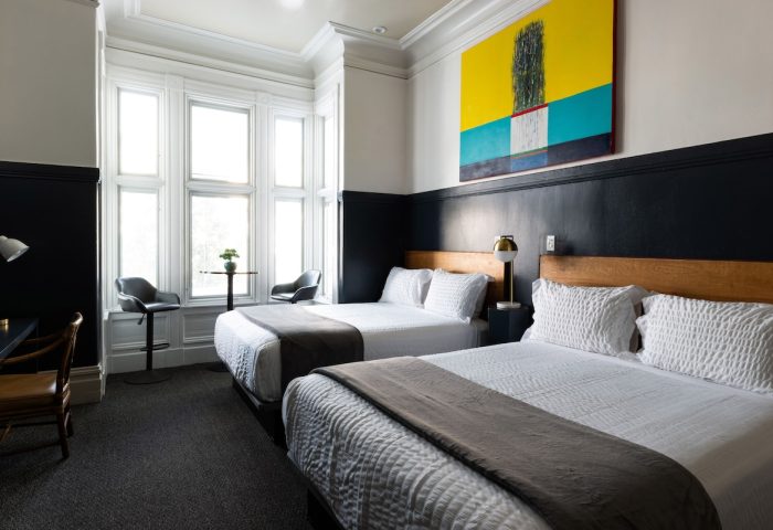 The Metro Hotel's gay-friendly room with two beds, a desk, and a window seating area. Modern art adorns the wall. Comfortable stay.