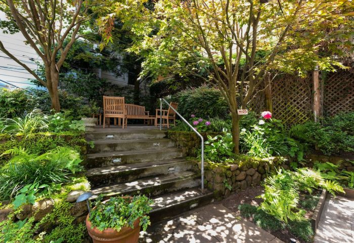 The Metro Hotel's gay-friendly garden. Stone steps lead to benches under trees. Lush greenery and flowers create a tranquil, welcoming space.