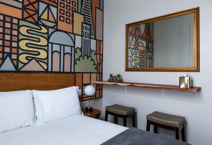 The Metro Hotel's gay-friendly room featuring a bed, stools, and a colorful mural. A mirror reflects the abstract city design.