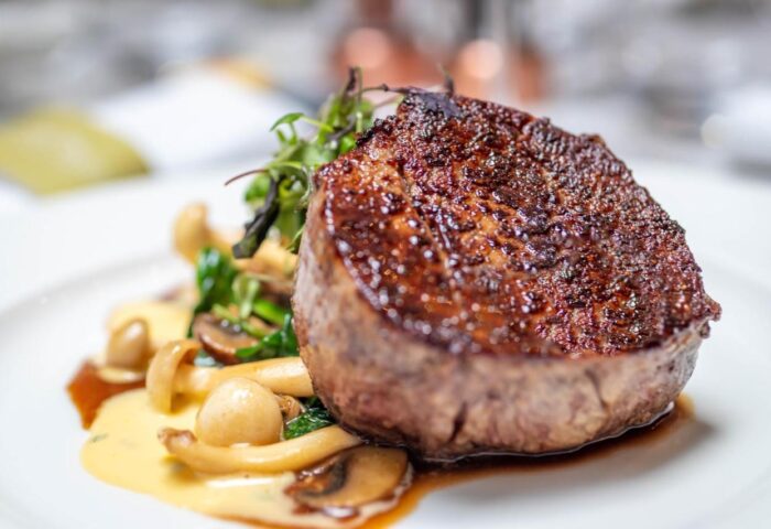Fine dining at The Morgan Hotel, a gay-friendly hotel. A juicy steak sits atop mushrooms and greens, promising a delicious culinary experience.