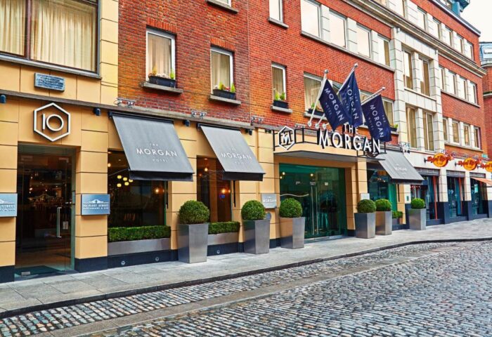 Facade of The Morgan Hotel, a gay-friendly hotel in Dublin. Flags bearing the hotel's name adorn the entrance. Potted plants add greenery.