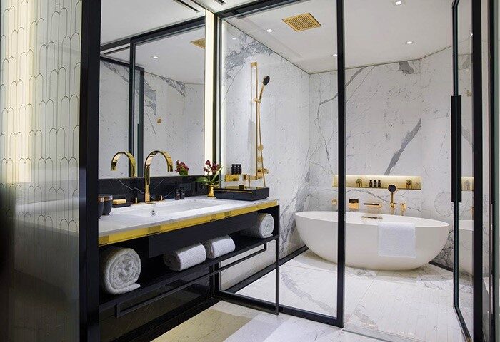 The Murray Hong Kong, a Niccolo Hotel bathroom. Gay-friendly hotel with a luxurious bathtub and gold fixtures, marble walls.