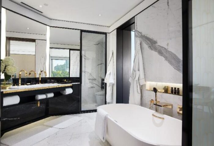 The Murray, Hong Kong, a Niccolo Hotel bathroom. Luxurious design with a tub, marble walls, and gold fixtures. Gay-friendly hotel bathroom.