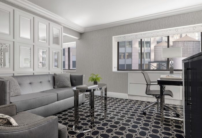 The Muse New York, a gay-friendly hotel: Room interior with a gray sofa, desk, and NYC view. Modern design, perfect for gay travelers.
