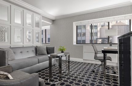 The Muse New York, a gay-friendly hotel: Room interior with a gray sofa, desk, and NYC view. Modern design, perfect for gay travelers.