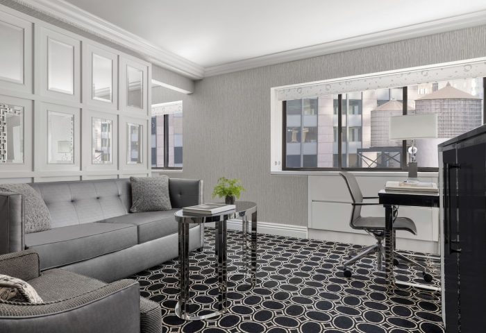The Muse New York, a gay-friendly hotel: Room interior with a gray sofa, desk, and NYC view. Modern design, perfect for gay travelers.