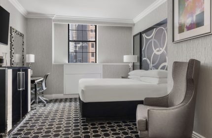 The Muse New York, a gay-friendly hotel: Guest room interior with bed, chair, desk, and city view. Modern design for gay travel.