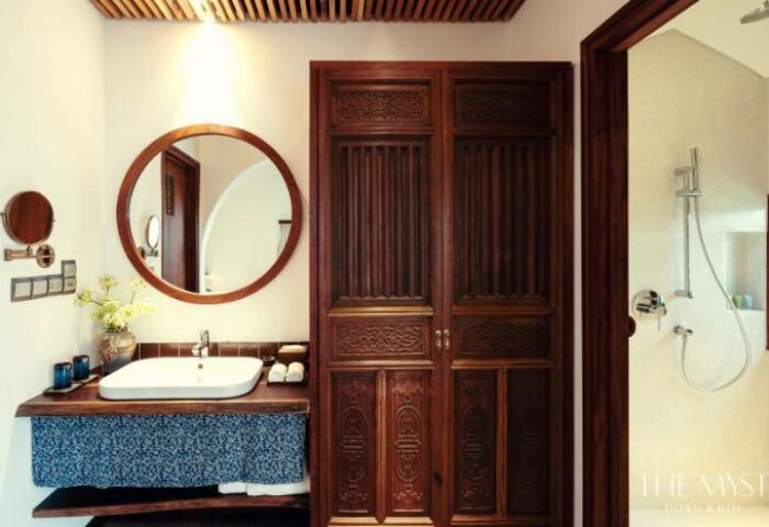 The Myst Dong Khoi gay-friendly hotel: Bathroom with sink, round mirror, carved wooden door, and shower. Luxury travel in Ho Chi Minh City.