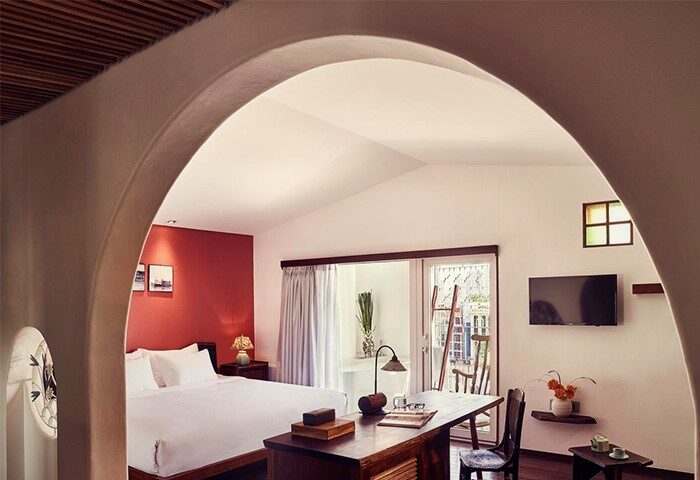 The Myst Dong Khoi gay-friendly hotel room. Archway view of bed, desk, and balcony. Modern design meets Vietnamese charm for gay travelers.
