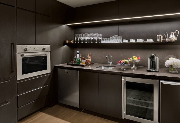 Kitchenette at The New York EDITION, a gay-friendly hotel. Dark cabinets, oven, sink, wine fridge, and shelf with glassware. Upscale amenities.