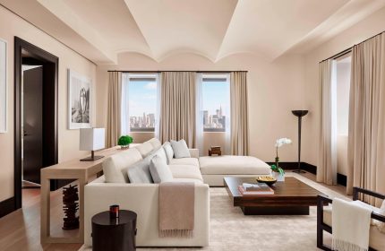 The New York EDITION hotel suite. Living area with a large sofa, coffee table, and city views. Gay-friendly hotel, luxury travel.