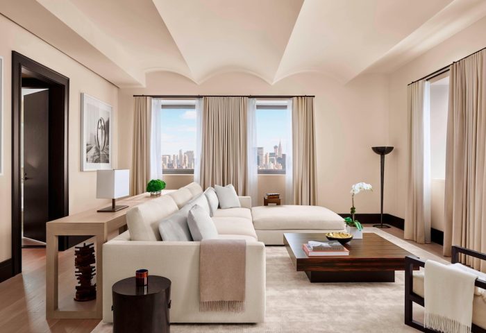 The New York EDITION hotel suite. Living area with a large sofa, coffee table, and city views. Gay-friendly hotel, luxury travel.