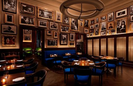 Dining area at The New York EDITION, a gay-friendly hotel. Walls covered in framed photos, blue seating, and warm lighting create an intimate vibe.