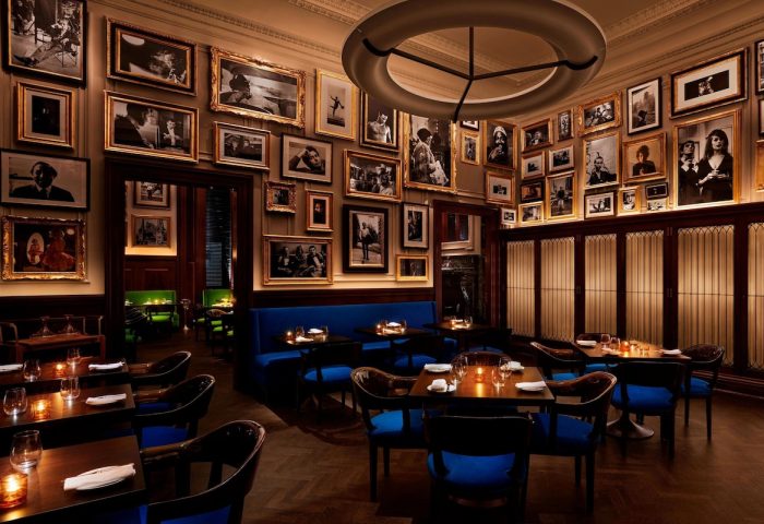 Dining area at The New York EDITION, a gay-friendly hotel. Walls covered in framed photos, blue seating, and warm lighting create an intimate vibe.