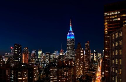 Night view of The New York EDITION, a gay-friendly hotel. The Empire State Building is illuminated in blue, part of the NYC skyline.