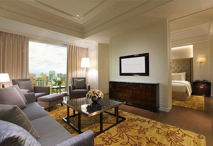 The Okura Prestige Taipei Hotel suite living room. Gay-friendly hotel with city view, sofa, TV, and bedroom access. Luxury Taiwan travel.