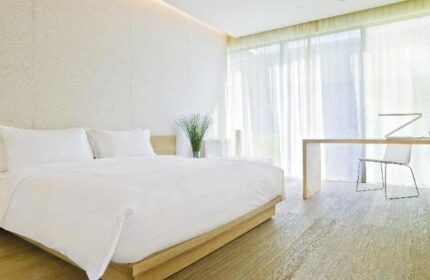 Minimalist room at The Opposite House Hotel, a gay-friendly hotel. Features a large bed, desk, and sheer curtains. Modern, clean design.