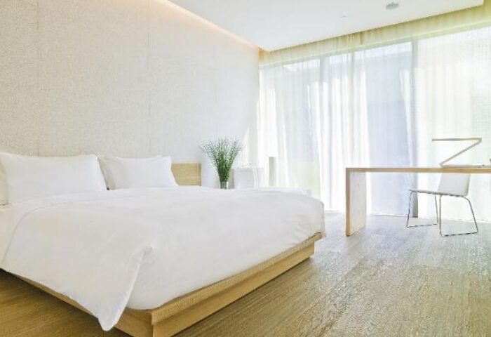 Minimalist room at The Opposite House Hotel, a gay-friendly hotel. Features a large bed, desk, and sheer curtains. Modern, clean design.