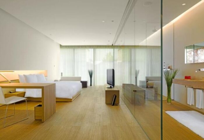 The Opposite House Hotel room. Gay-friendly hotel bedroom with bed, desk, TV, and glass-enclosed bathroom. Modern design.
