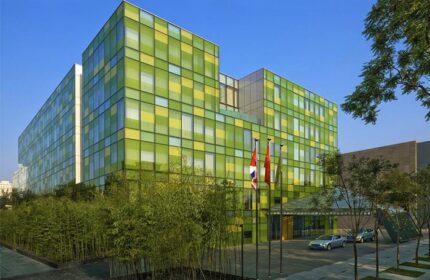 The Opposite House Hotel exterior. Gay-friendly hotel with a green and yellow facade. Modern architecture, trees, and cars outside.