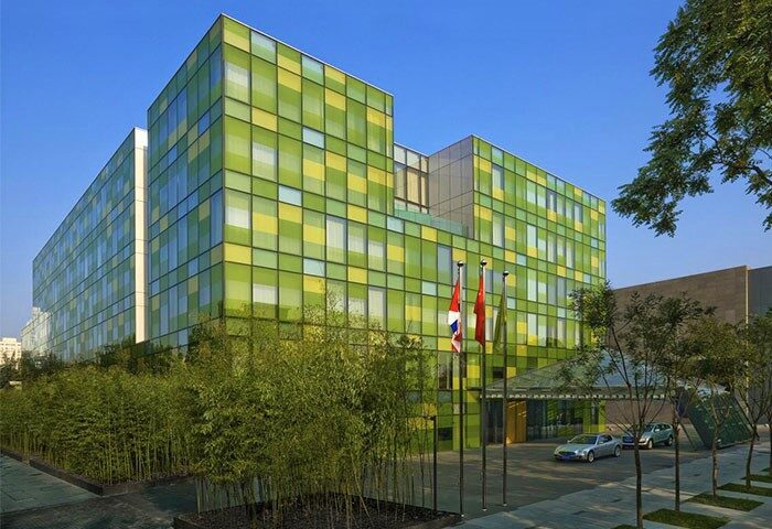 The Opposite House Hotel exterior. Gay-friendly hotel with a green and yellow facade. Modern architecture, trees, and cars outside.