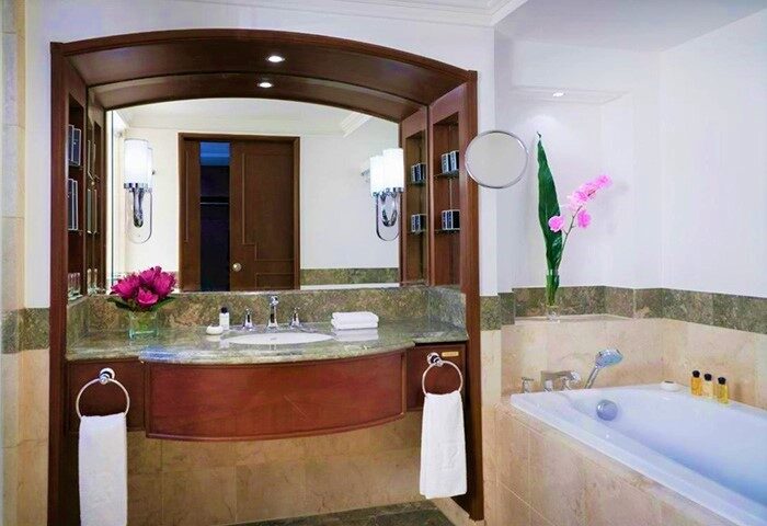 Bathroom at The Peninsula Manila, a gay-friendly hotel. Features a marble countertop, vanity mirror, bathtub, & upscale amenities.