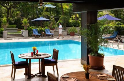 Poolside view at The Peninsula Manila, a gay-friendly hotel. Tables and chairs overlook the pool and lush greenery, perfect for relaxation.