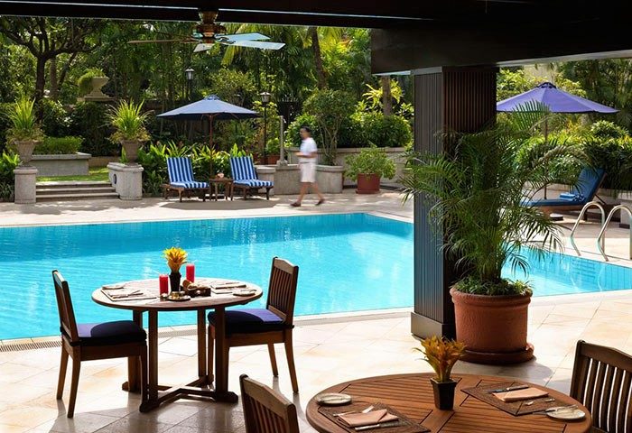 Poolside view at The Peninsula Manila, a gay-friendly hotel. Tables and chairs overlook the pool and lush greenery, perfect for relaxation.