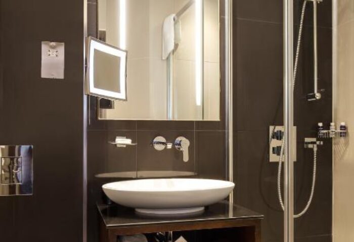 Bathroom at The Piccadilly London West End, a gay-friendly hotel. Modern design with a large mirror, vessel sink, and walk-in shower.