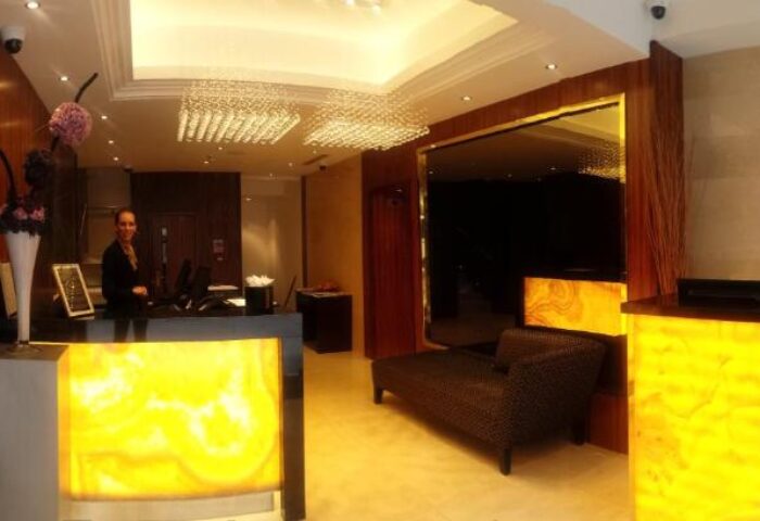 Hotel reception at The Piccadilly London West End, a gay-friendly hotel. Check-in desk with staff, seating area, and elegant lighting. Upscale ambiance.