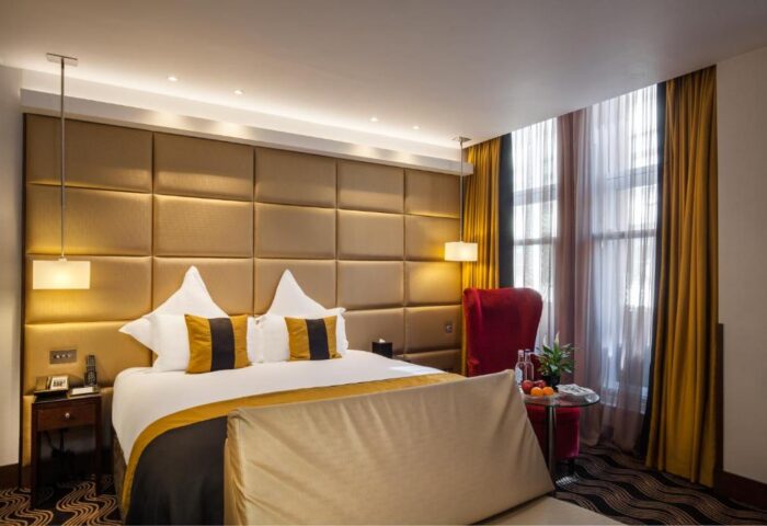 Piccadilly London West End gay-friendly hotel room. Modern design with a padded headboard, stylish pillows, and accent chair. Upscale lodging.