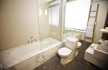 Bathroom at The Prince Hotel, a gay-friendly hotel. Bathtub with glass partition, toilet, sink, and ladder with towels. Modern design.