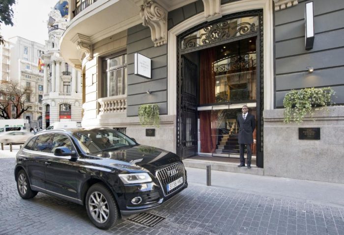 Facade of The Principal Madrid Hotel, a gay-friendly hotel. A black car is parked outside. Doorman standing at the entrance.