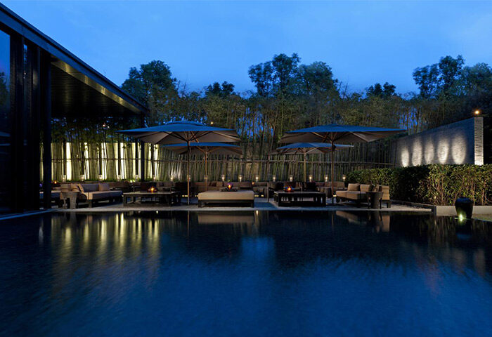 The PuLi Hotel and Spa gay-friendly hotel outdoor pool area at dusk. Lounge seating, umbrellas, bamboo and lighting create a serene ambiance.