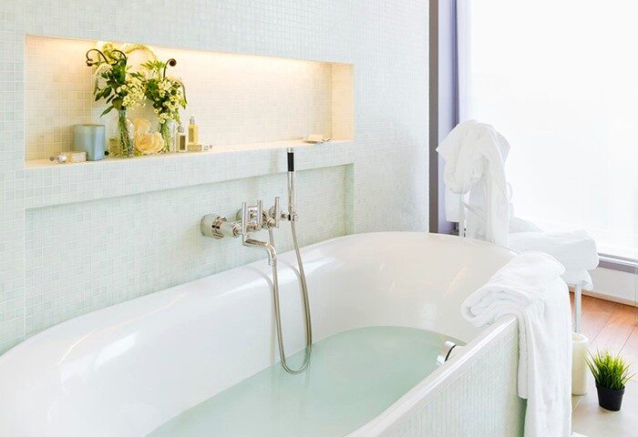 The Putman gay-friendly hotel bathroom. White tub filled, chrome fixtures, flowers, and toiletries on a shelf. Relaxing bath at The Putman.