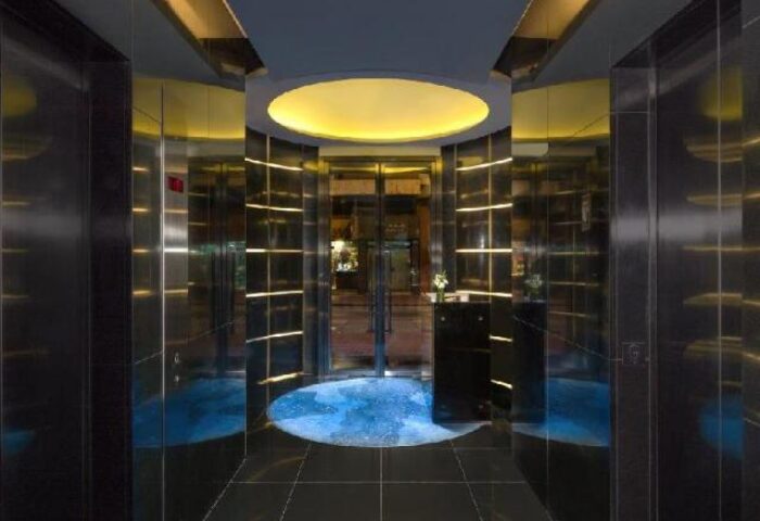 The Putman gay-friendly hotel elevators. Stylish interior with black tiled floor, mirrored walls, and circular blue water feature. Modern design.