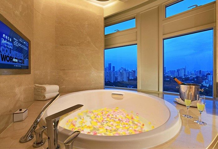 Radisson Collection Hotel Xing Guo Shanghai bathtub with flower petals, champagne, and city view. Gay-friendly hotel bathroom interior.