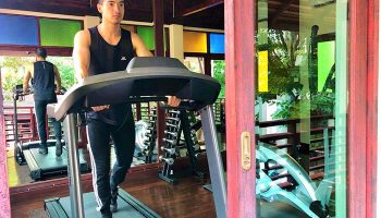Gay-Friendly The Rim Chiang Mai Hotel gym. Man on treadmill. Fitness center at this gay travel destination in Thailand. Weights visible.