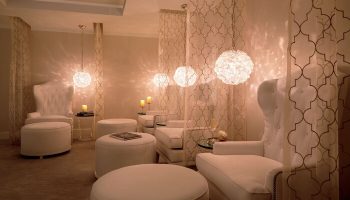 The Ritz-Carlton Rancho Mirage gay-friendly hotel spa. White lounge chairs and ottomans under decorative lights and curtains. Relaxing space.