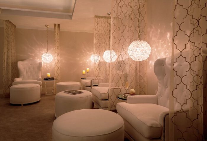 The Ritz-Carlton Rancho Mirage gay-friendly hotel spa. White lounge chairs and ottomans under decorative lights and curtains. Relaxing space.
