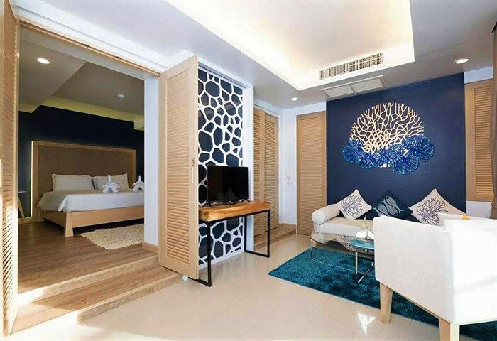 Royal Palm Beachfront Hotel suite: Living area with sofa, TV, and bedroom view. Gay-friendly hotel design with ocean-themed decor.