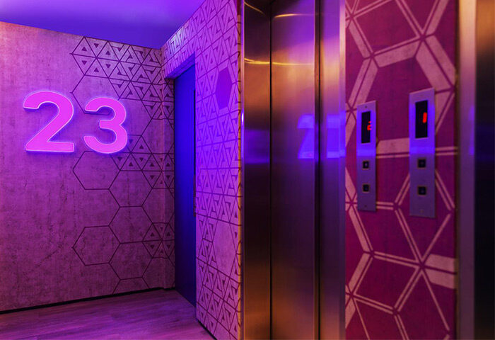 The Sheung Wan hotel's stylish elevator lobby. Geometric patterns adorn the walls, illuminated by neon lights. A modern, gay-friendly hotel design.
