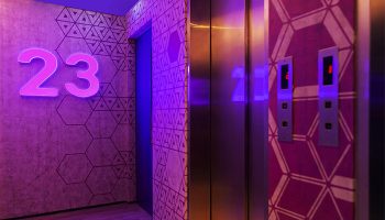 The Sheung Wan hotel's stylish elevator lobby. Geometric patterns adorn the walls, illuminated by neon lights. A modern, gay-friendly hotel design.