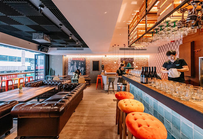 Interior of The Sheung Wan, a gay-friendly hotel in Hong Kong. The bar area features leather seating, a brick wall, and a bartender.